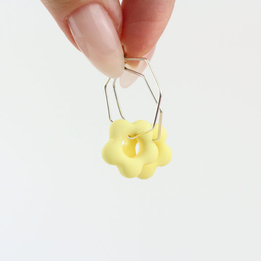 Sechseckige silberne Creole mit einem bunten Anhänger in Form einer Blume.